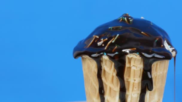 Chocolate sauce icing flows over ice cream in a waffle cup on blue background — Stock Video