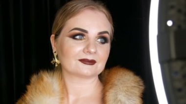 Fox Kürk ve stüdyoda siyah arka planda poz büyük altın küpe bir kat altın makyaj ve dumanlı gözleri ile yağ kadın modeli