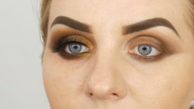 Master makyaj sanatçısı mavi gözlü şişman bir kadın modeli güzellik salonunda profesyonel makyaj altın dumanlı gözleri uygulamak