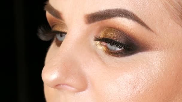 Beautiful fat woman model with gold makeup, smoky eyes dark red lipstick false eyelashes and blue eyes posing on a black background in studio. Face close up view — Stock Video
