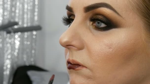 Profesjonalny mistrz makijaż artysta stosuje ciemne czerwone szminki na modelu cienkie usta ze specjalnym pędzlem i makijażu smoky eyes w salonie piękności — Wideo stockowe