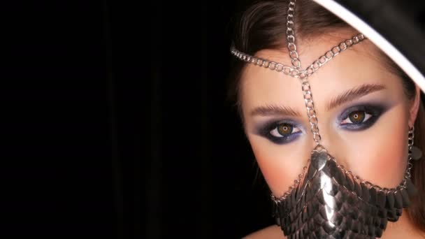 Girl model in unusual iron stylish muzzle. Symbol of the silence of a woman. Sexy tender beautiful young girl model with long hair and blue evening make-up smoky eyes — Stock Video