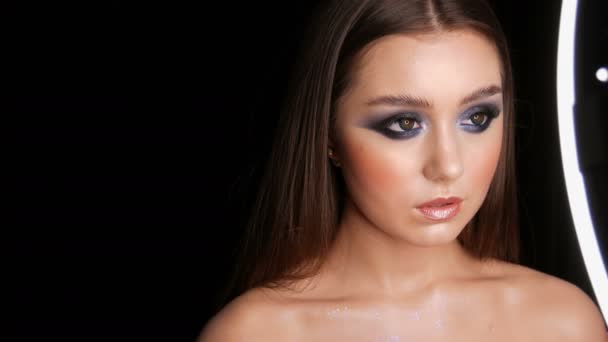 Gyönyörű szexi fiatal lány, esti kék make-up füstös szeme hosszú haj és a kozmetikai színes kontaktlencsék pózol a modell stúdióban a fekete háttér — Stock videók