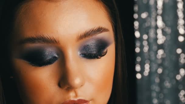 Sexy macio belo modelo jovem com cabelos longos e azul à noite make-up olhos fumegantes posando na frente da câmera no fundo preto. Modelo de menina com pestanas longas e largas sobrancelhas flerta — Vídeo de Stock