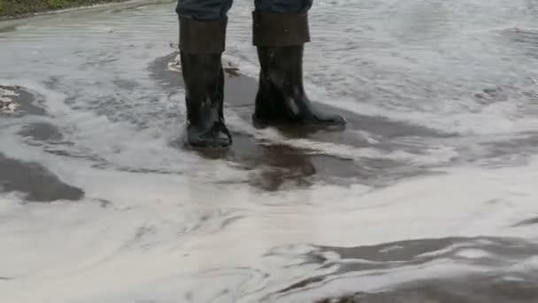 灾难。村子里洪水泛滥。肮脏的黑河沿着道路流淌。穿着黑色橡胶靴的男人穿过水坑. — 图库视频影像