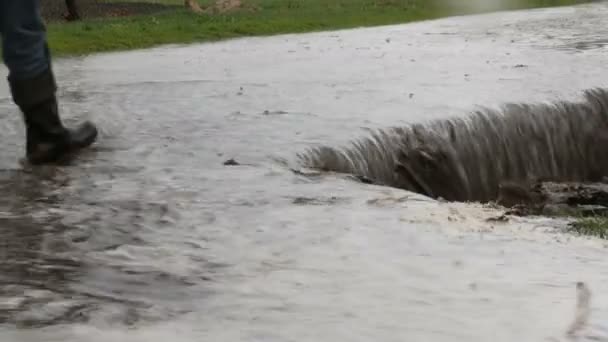 Un desastre. Inundaciones en el pueblo. Ríos negros sucios fluyen a lo largo de la carretera. Hombre con botas de goma negro camina a través de los charcos . — Vídeos de Stock