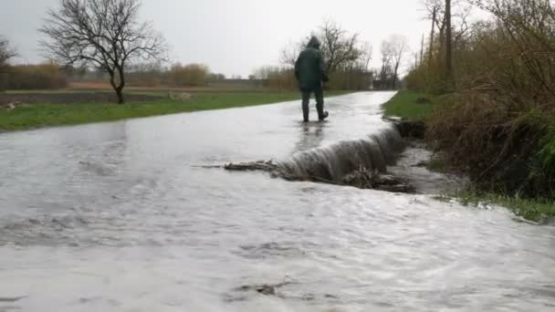 Katastrofy. Zaplavení ve vesnici. Podél silnice protékají špinavé černé řeky. Člověk v černých gumových botách prochází loukami. — Stock video