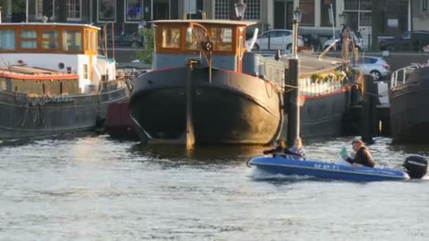 Amsterdam, Niederlande - 21. April 2019: Touristen fahren mit dem Boot auf dem Amsterdam-Kanal, auf dem festgemachte Boote liegen. authentische holländische Häuser und Straßen der Hauptstadt der Niederlande — Stockvideo