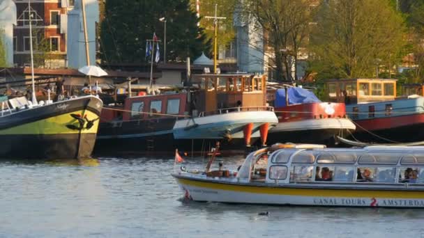 Amsterdam, Nizozemsko-21. dubna 2019: turisté se plaví lodí po amsterdamském průplavu, kde se nacházejí lodě s kotvími. Autentické nizozemské domy a hlavní ulice Nizozemska — Stock video