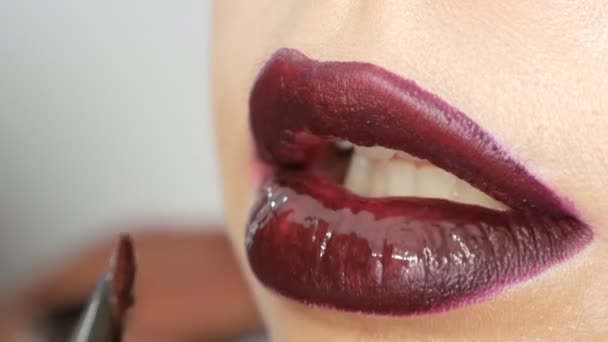 Jugosos labios rojos negros oscuros se componen con lápiz labial de cepillo especial y brillo de labios, que se aplica por el artista de maquillaje profesional. Alta moda, chica modelo labios de cerca ver — Vídeo de stock