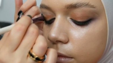 Kadın makyaj sanatçısı stilist genç modelin özel makyaj fırçası ile makyaj moda pembe dumanlı gözler yapar