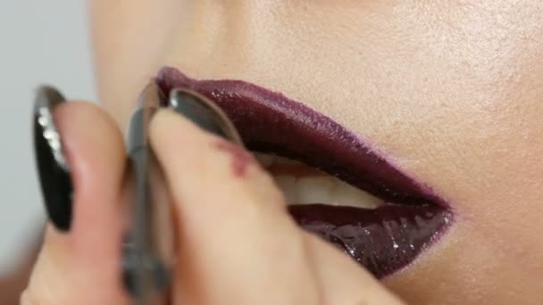 Jugosos labios rojos negros oscuros se componen con lápiz labial de cepillo especial y brillo de labios, que se aplica por el artista de maquillaje profesional. Alta moda, chica modelo labios de cerca ver — Vídeos de Stock