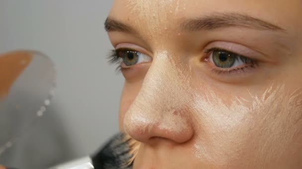 Un maquillador profesional aplica un corrector a la modelo de niña con un cepillo especial. Alta moda, el rodaje de vídeo en el estudio — Vídeo de stock