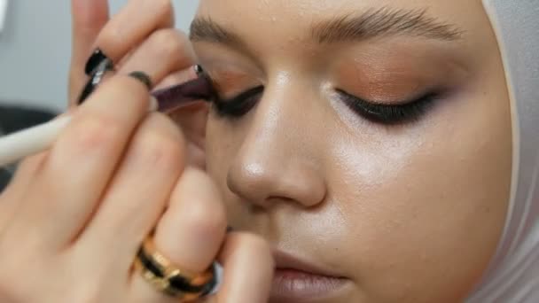 Woman make-up artist stylist makes makeup fashionable pink smoky eyes with special makeup brush of young model — Stock Video