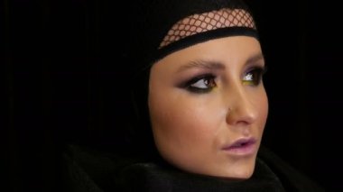 Güzel makyaj ile profesyonel kız modeli siyah dul görüntüsünde siyah arka planda kameranın önünde kafasına siyah bir kap içinde pozlar. Yüksek moda