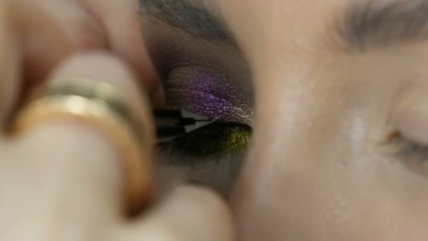 Artista de maquillaje profesional pega pestañas negras largas falsas en el ojo modelo, que se colorea con diferentes sombras de ojos de color . — Vídeo de stock