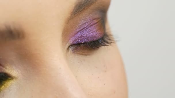 Camaleón de sombra de ojos multicolor de moda con color amarillo púrpura gris plateado en el párpado de la hermosa modelo de niña con ojos marrones. Maquillaje cosmético profesional. Ojo de cerca vista — Vídeo de stock