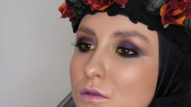 Professioneel meisje model met mooie make-up poses in een zwarte pet en krans op haar hoofd in de voorkant van de camera in het beeld van Black Widow. High-Fashion — Stockvideo