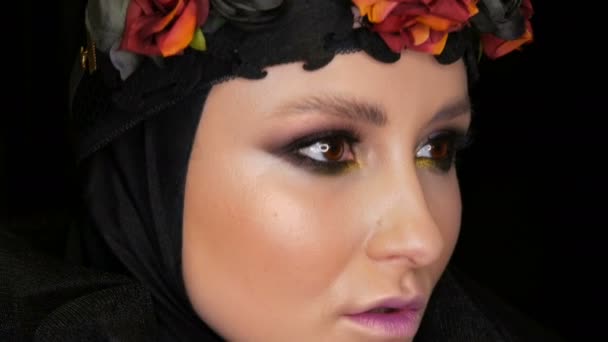 Επαγγελματική κορίτσι μοντέλο με όμορφο μακιγιάζ θέτει σε μια μαύρη cap και στεφάνι στο κεφάλι της μπροστά από την κάμερα σε μαύρο φόντο με την εικόνα του μια μαύρη χήρα. Υψηλός-μόδας — Αρχείο Βίντεο