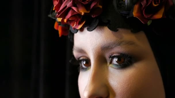 Профессиональная девушка-модель с красивым макияжем позирует в черной шапке и венке на голове перед камерой на черном фоне на изображении черной вдовы. Высокая мода — стоковое видео