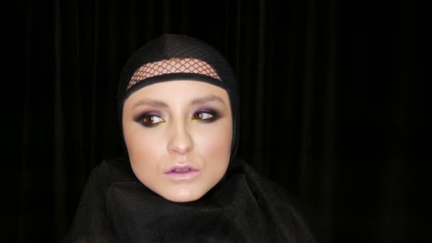 Profesionální dívčí model s nádherným make-upem představuje v černé čepici na hlavě před kamerou na černém pozadí v obraze černé vdovy. High-móda — Stock video
