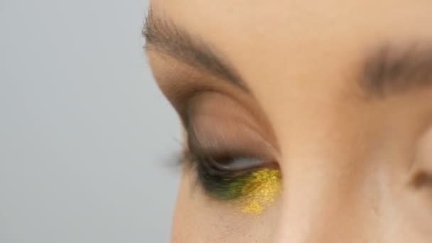Модна різнокольорова тінь для очей хамелеон з жовтим фіолетовим сірим срібним кольором на повіці красивої дівчинки моделі з коричневими очима. Професійний косметичний макіяж. Око крупним планом — стокове відео