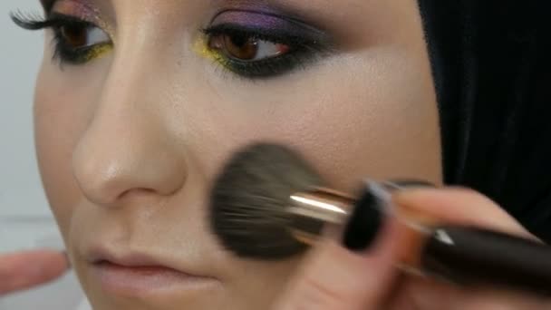 Un artista profesional hace maquillaje a un hermoso modelo de niña, polvo de plumas, iluminador, crema de fundación con cepillo especial para el maquillaje — Vídeos de Stock