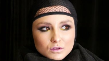 Güzel makyaj ile profesyonel kız modeli siyah dul görüntüsünde siyah arka planda kameranın önünde kafasına siyah bir kap içinde pozlar. Yüksek moda