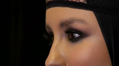 Güzel makyaj ile profesyonel kız modeli siyah dul görüntüsünde siyah arka planda kameranın önünde kafasına siyah bir kap içinde pozlar. Yüksek moda
