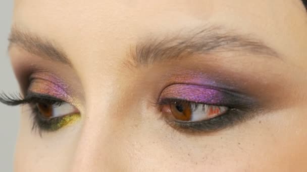 Модный разноцветный хамелеон тени для глаз с желтым фиолетово-серым серебристым цветом на веку красивой девушки-модели с карими глазами. Профессиональная косметическая косметика. Вид вблизи глаз. — стоковое видео