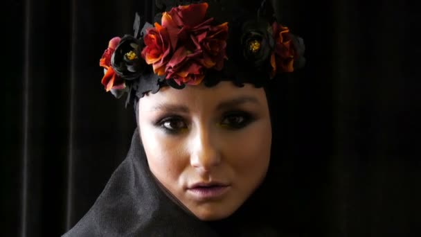 Modèle de fille professionnelle avec de belles poses de maquillage dans une casquette noire et une couronne sur sa tête devant la caméra sur fond noir à l'image d'une veuve noire. Haute couture — Video