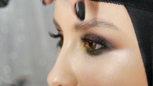 Artista de maquillaje profesional pega pestañas negras largas falsas en el ojo modelo, que se colorea con diferentes sombras de ojos de color . — Vídeos de Stock