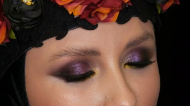 Professional girl model with beautiful makeup poses in a black cap and wreath on her head in front of the camera on black background in the image of a black widow. High-fashion — Stock Video