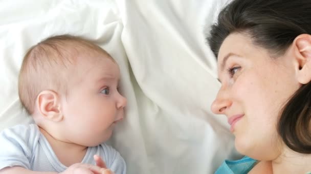 Fiatal szép anya, hosszú, Sötét haja fekszik egy fehér ágyban, és játszik az újszülött két hónapos — Stock videók