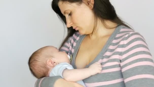 Joven hermosa madre con el pelo largo y oscuro está sosteniendo un bebé recién nacido de dos meses sobre fondo blanco en el estudio — Vídeos de Stock