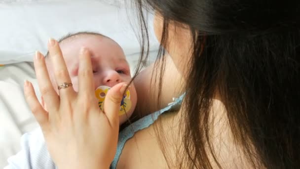 Une belle jeune mère aux cheveux longs touche doucement et berce son nouveau-né dans les bras tout en étant assise sur son lit. Les enfants face au gros plan vue — Video