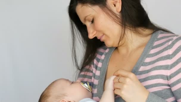 Jonge mooie moeder met lang donker haar houdt een pasgeboren baby van twee maanden op witte achtergrond in Studio — Stockvideo