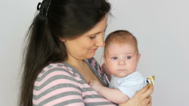 Joven hermosa madre con el pelo largo y oscuro está sosteniendo un bebé recién nacido de dos meses sobre fondo blanco en el estudio — Vídeo de stock