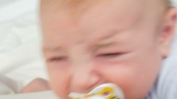 Δύο μηνών νεογέννητο μωρό κλαίει δυνατά με την πιπίλα στο στόμα. Παιδικό πρόσωπο κοντά στην προβολή — Αρχείο Βίντεο