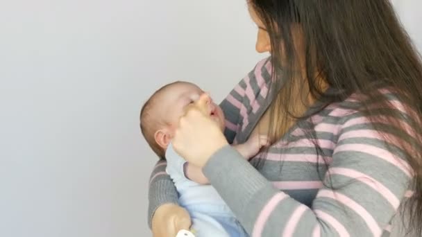 Giovane bella madre con lunghi capelli scuri sta tenendo un neonato di due mesi su sfondo bianco in studio — Video Stock