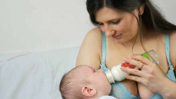 Um bebê recém-nascido de dois meses está nos braços da mãe e chupa um mamilo de uma mamadeira de leite — Vídeo de Stock