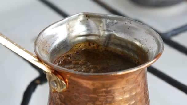 El café negro molido en un turco de cobre se prepara y hierve en una estufa de gas. Barista preparando sabrosa bebida caliente en casa — Vídeo de stock