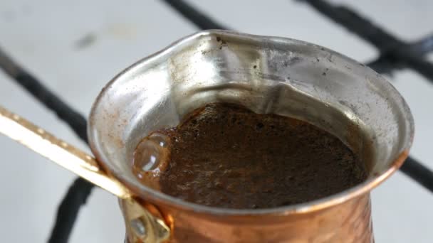 Глиняный черный кофе в медном турке варится и закипает на газовой плите. Бариста готовит горячий вкусный напиток дома крупным планом — стоковое видео