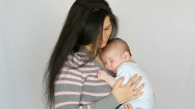 Uzun koyu saçlı genç güzel anne stüdyoda beyaz arka plan üzerinde iki aylık yeni doğmuş bir bebek bebek tutuyor