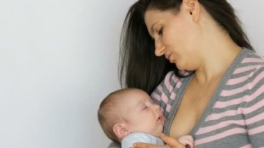 Uzun koyu saçlı genç güzel anne stüdyoda beyaz arka plan üzerinde iki aylık yeni doğmuş bir bebek bebek tutuyor