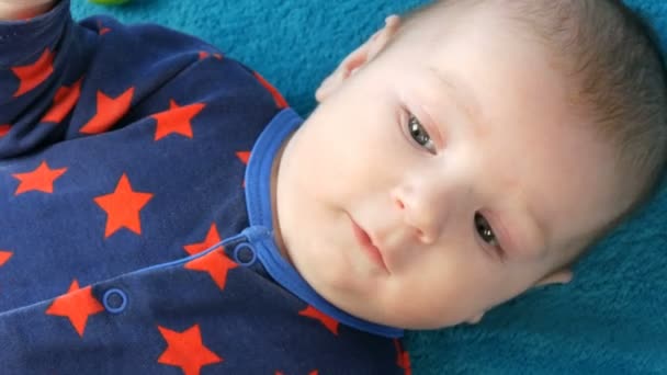 Портрет красивого смешного новорожденного малыша двух месяцев, лежащего на синем покрывале в окружении детской дребезги — стоковое видео