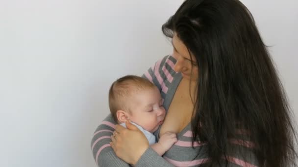 Jovem mãe bonita com cabelos longos escuros está segurando um bebê recém-nascido de dois meses em fundo branco no estúdio — Vídeo de Stock