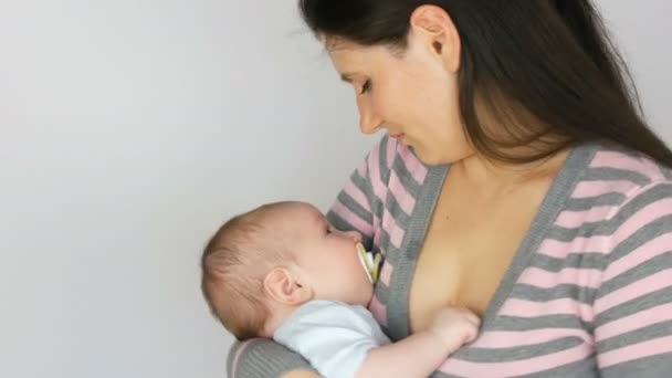 Jovem mãe bonita com cabelos longos escuros está segurando um bebê recém-nascido de dois meses em fundo branco no estúdio — Vídeo de Stock