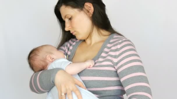 長い黒髪の若い美しい母親は、スタジオで白い背景に2ヶ月の新生児の赤ちゃんを保持しています — ストック動画