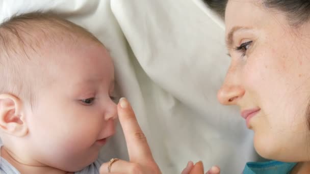 Uzun koyu saçlı genç güzel anne beyaz bir yatakta yatıyor ve iki aylık yeni doğan bebek ile oynuyor — Stok video